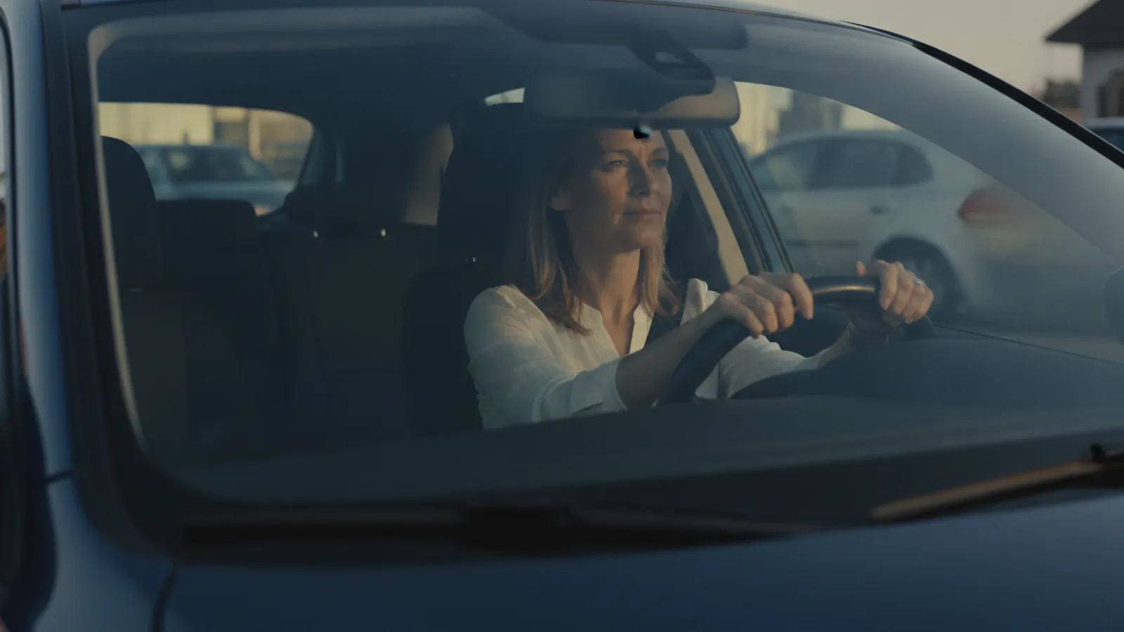 A driver sits at the wheel of a stationary car in soft daylight, both hands on the rim, looking ahead.