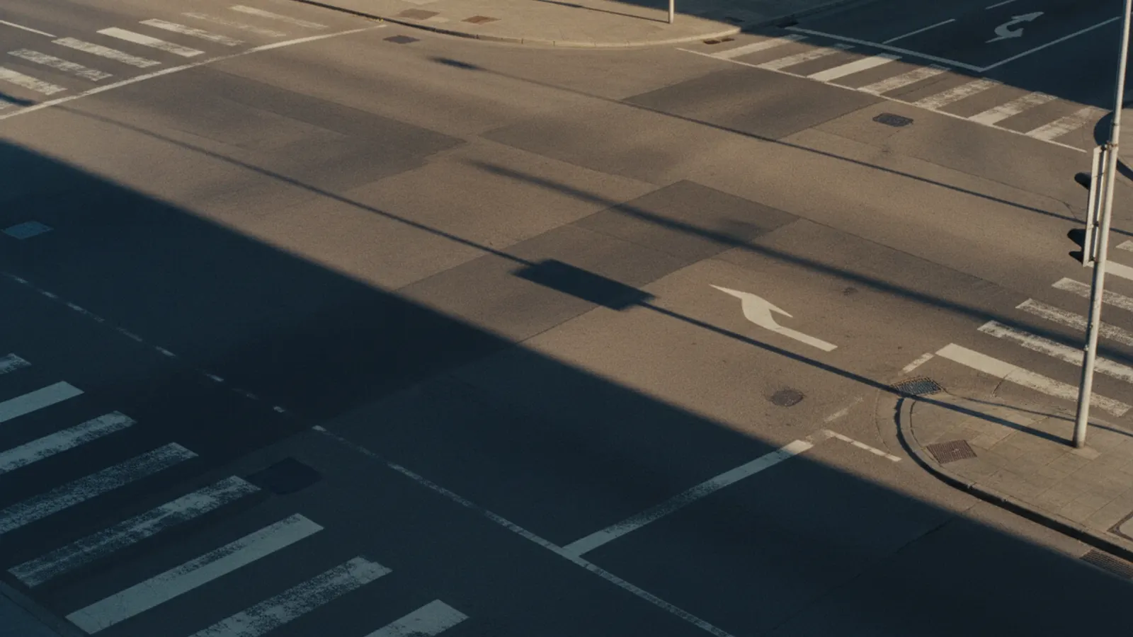 An empty four-way junction at the end of the afternoon, long shadows crossing the worn road markings.